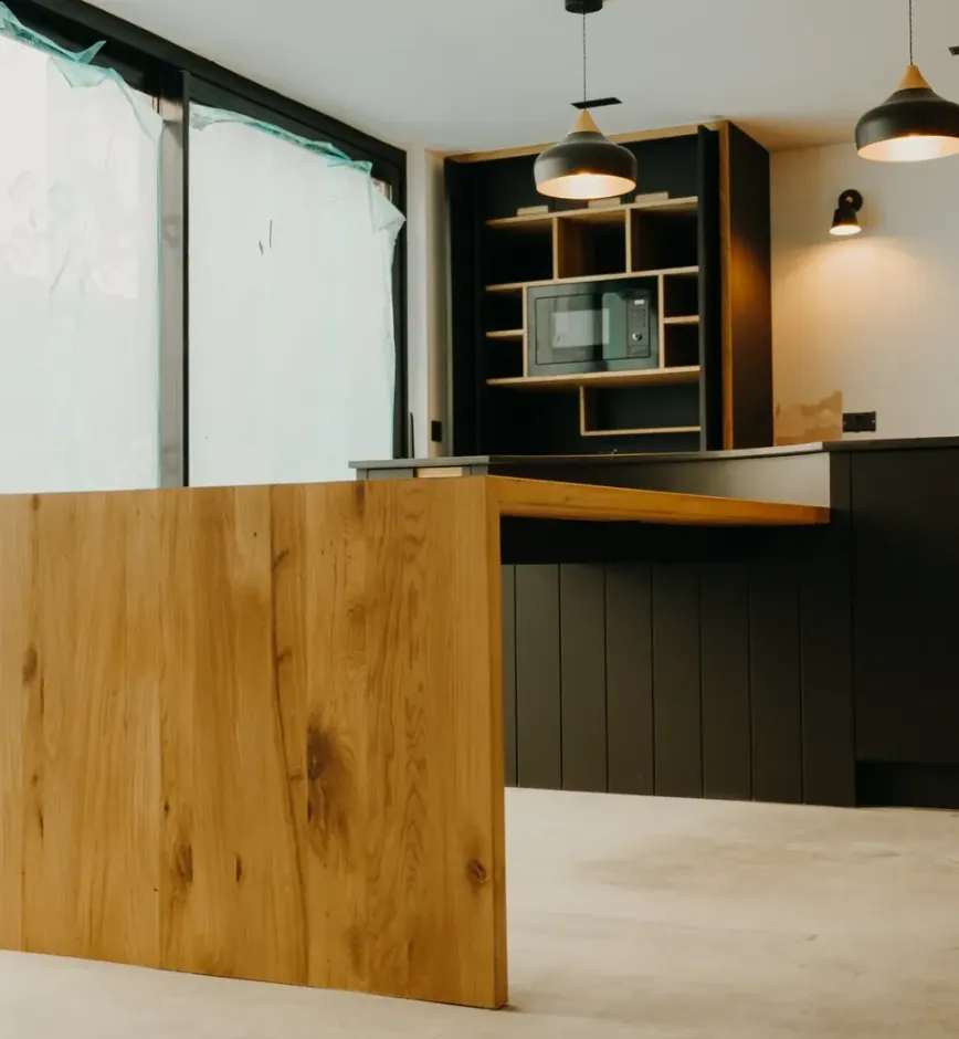 Cantilevered oak breakfast bar extending from matte black kitchen units