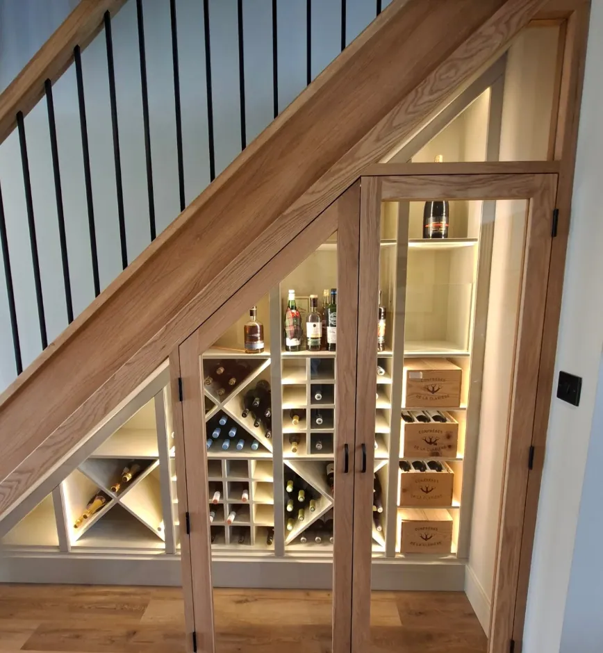 Custom oak under-stairs wine storage unit with glass-fronted doors and warm LED lighting
