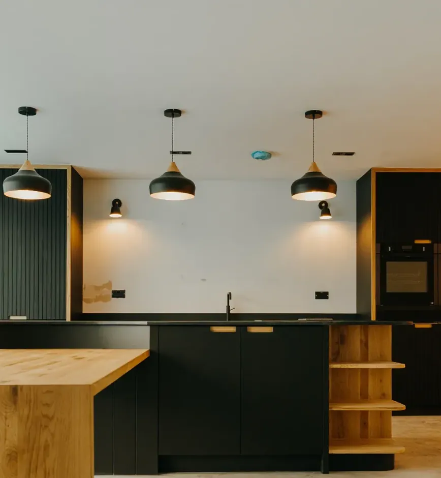 Oak breakfast bar in front of black cabinets and open oak shelving