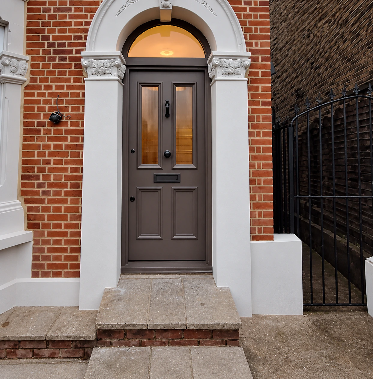 Panelled dark wood front door set within a white neoclassical arched entrance on a brick townhouse