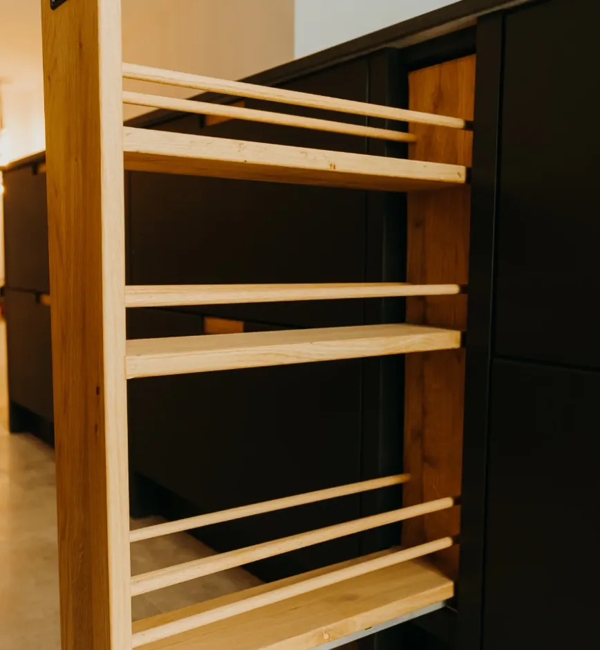 Pull-out oak spice rack next to matte black reeded cabinets