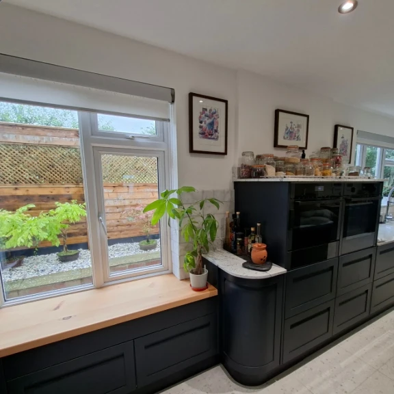 Knock-through kitchen with dark shaker units, curved end unit and oak window seat